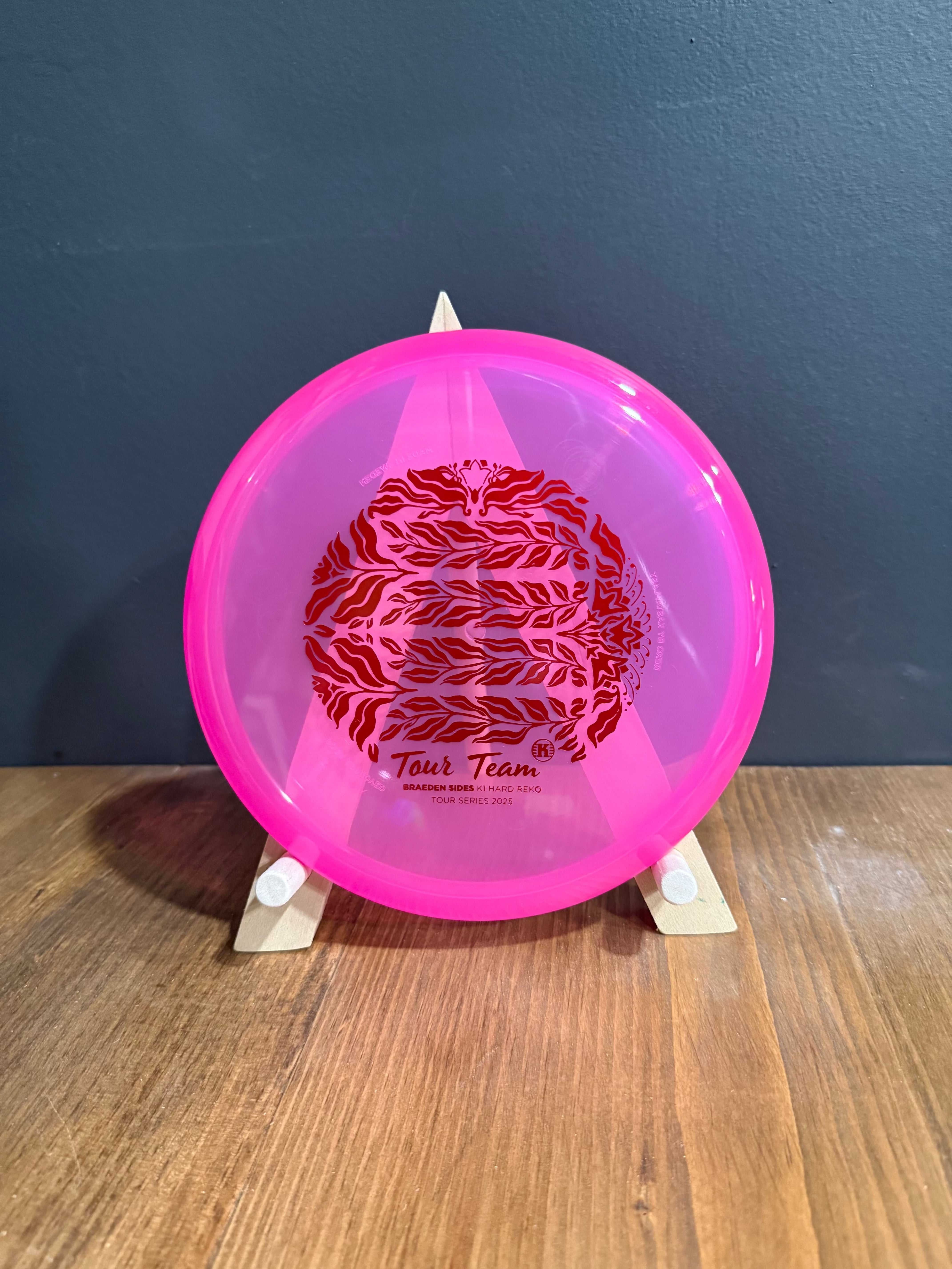 K1 Hard Reko disc golf putter in translucent bright pink plastic with red tree-themed team stamp and rounded profile