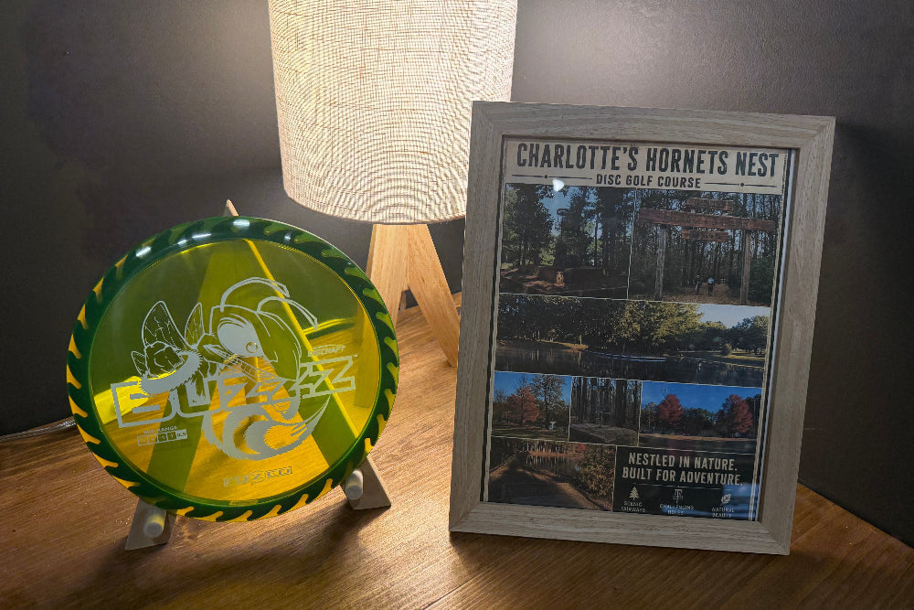 Handcrafted Disc Holders in green translucent acrylic with graphic design, beside a grey wooden framed disc golf print
