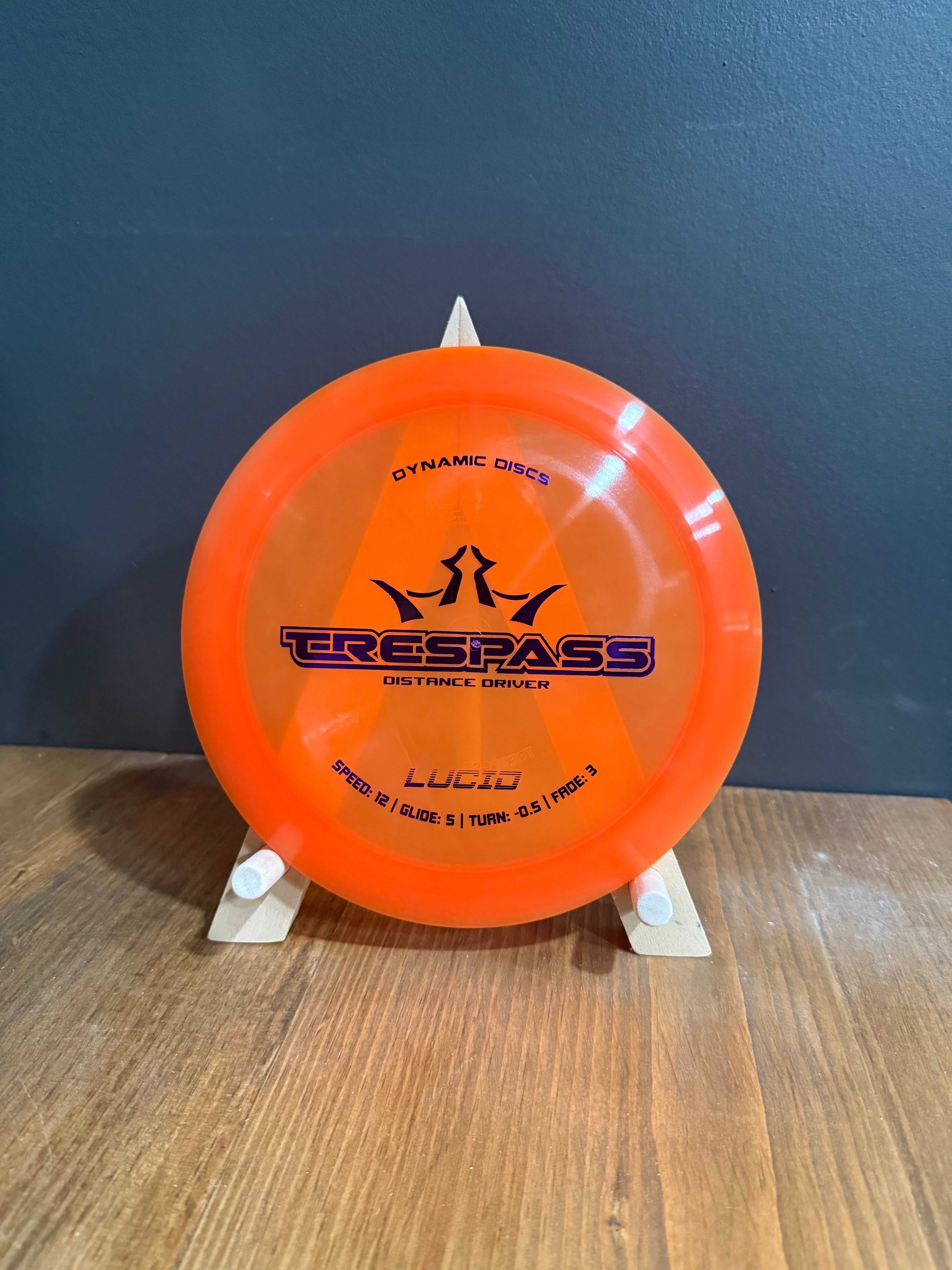 Lucid Trespass orange golf disc with translucent plastic, black graphics, and wide high-speed driver rim